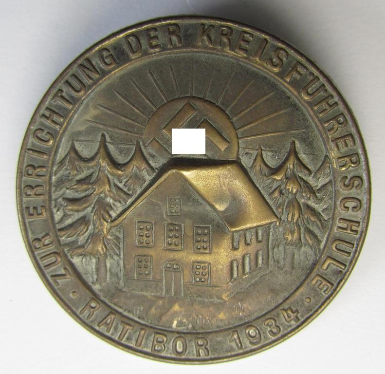 Commemorative - and truly unusally seen! - bronze-coloured, N.S.D.A.P.-related 'tinnie' depicting a detailed illustration of a house and swastika-sunburst surrounded by the text: 'Zur Errichtung der Kreisführerschule - Ratibor - 1934'