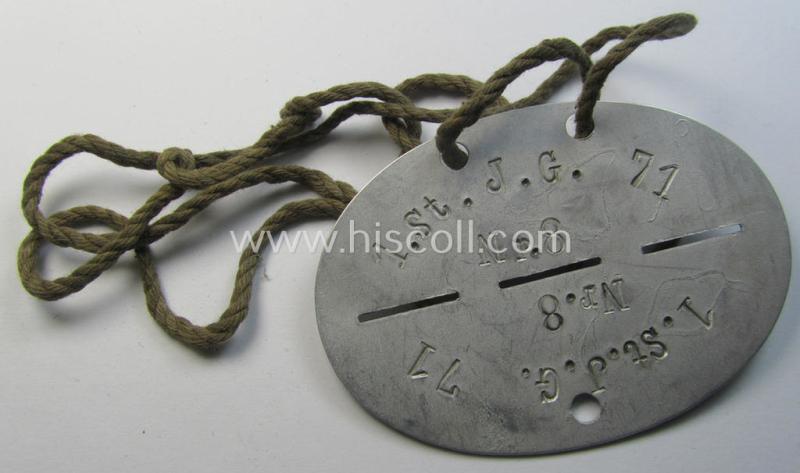 Attractive - and typical aluminium-based - WH (Luftwaffe o. Jagdgeschwader) related ID-disc (ie. 'Erkennungsmarke') bearing the stamped unit-designation that simply reads: '1.St. J.G.71' and that comes mounted onto its period cord as issued