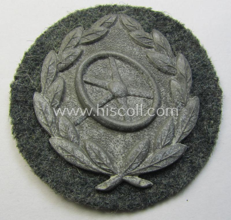 WH (Heeres- ie. Waffen-SS) so-called: 'Kraftfahrbewährungs-Abzeichen in Silber' (or: silver-class drivers' proficiency-badge) that comes mounted onto its piece of field-grey-coloured wool and that comes as probably issued- but never worn, condition