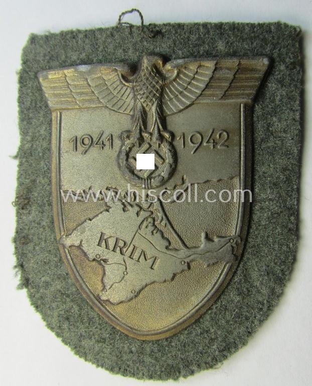 Attractive, WH (Heeres o. Waffen-SS) 'Krim'-campaign-shield that comes mounted onto its original, field-grey-coloured 'backing' and that comes in a surely issued-, minimally worn and/or (I deem) carefully tunic-removed-, condition