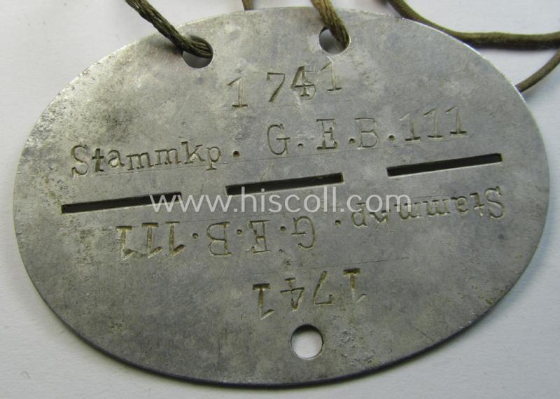 Attractive, aluminium-based WH (Heeres) (ie. 'Grenadiere'-related) ID-disc bearing the clearly stamped unit-designation that reads: 'Stammkp. G.E.B.111' and that comes still mounted onto its (period-attached) cord as issued- and/or worn