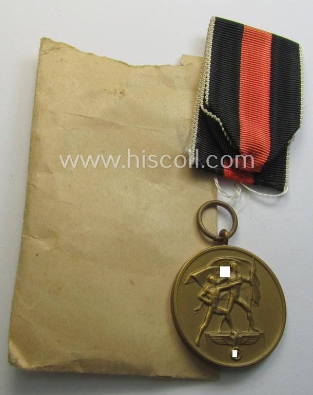 Neat, WH Czech occupation-medal '1 October 1938' and accompanying (minimally confectioned) ribbon (ie. 'Bandabschnitt') that comes stored in its original, carton-based pouch as was produced by the maker: 'Josef Bergs & Co.'
