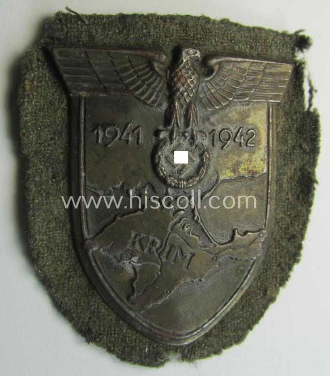 Truly worn, WH (Heeres o. Waffen-SS) 'Krim'-campaign-shield that comes mounted onto its original, field-grey-coloured 'backing' and that comes in a surely issued-, worn and/or carefully tunic-removed-, condition