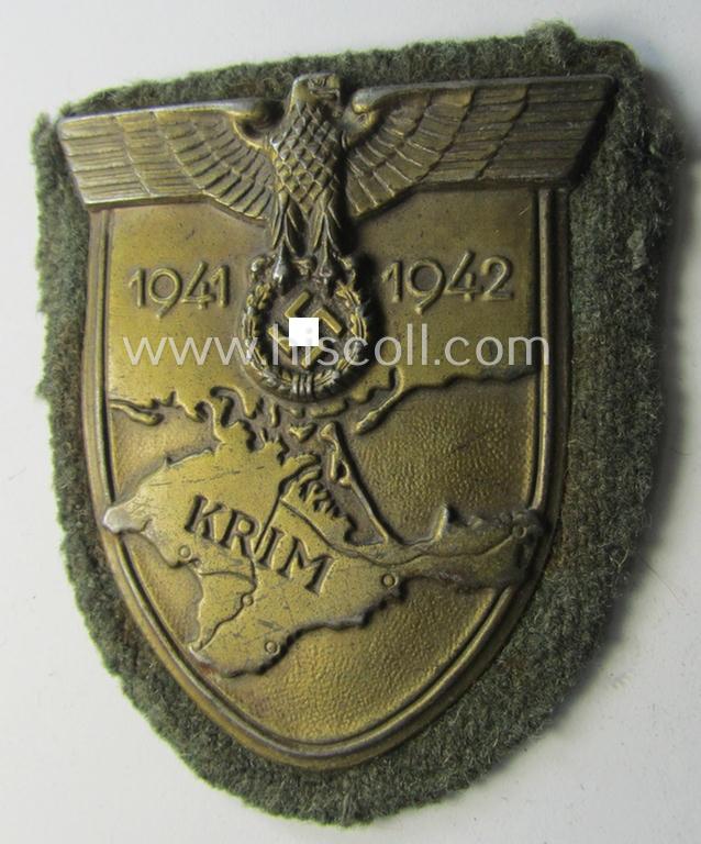 Truly worn, WH (Heeres o. Waffen-SS) 'Krim'-campaign-shield that comes mounted onto its original, field-grey-coloured 'backing' and that comes in a surely issued-, worn and/or carefully tunic-removed-, condition